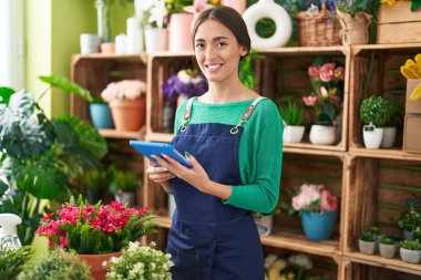 Young beautiful hispanic woman florist smiling confident using touchpad at flower shop