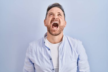 Middle age caucasian man standing over blue background angry and mad screaming frustrated and furious, shouting with anger. rage and aggressive concept. 