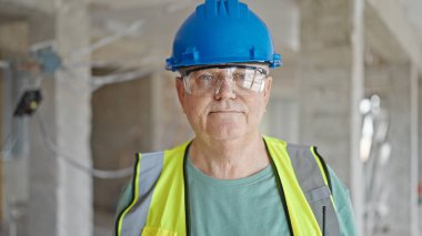 İnşaat alanında kendine gülen, orta yaşlı, gri saçlı bir inşaatçı.