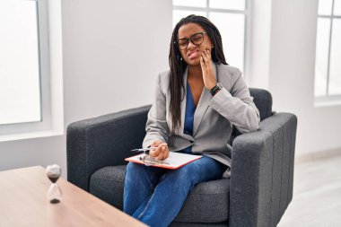 Saç örgüleriyle çalışan genç Afro-Amerikalı diş ağrısı ya da diş ağrısı yüzünden elleriyle ağıza dokunuyor. dişçi kavramı. 