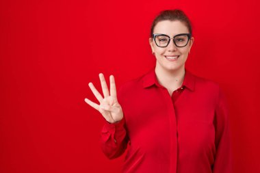 Kırmızı arka planda duran ve dört numaralı parmaklarıyla işaret eden, kendinden emin ve mutlu gülümseyen Latin kökenli genç kadın.. 