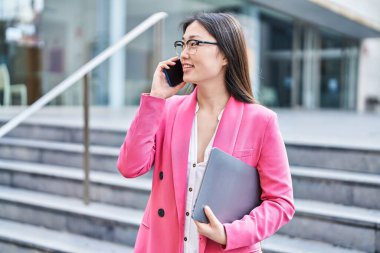 Çinli kadın iş adamı, elinde dizüstü bilgisayarla caddede konuşuyor.