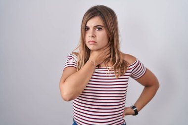 İzole edilmiş arka planda duran genç İspanyol kadın ağrılı boyuna dokunuyor, grip, mantar ve enfeksiyon yüzünden boğazı ağrıyor. 