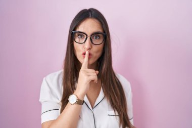 Genç esmer kadın pembe arka planda duran gözlüklü sessiz olmak istiyor. sessizlik ve gizli konsept. 