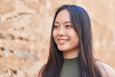 Genç Çinli kadın gülümsüyor. Kendinden emin. Caddenin kenarına bakıyor.