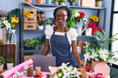 African american woman florist smiling confident using laptop at florist store