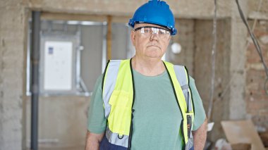 İnşaat alanında gevşek bir ifadeyle duran orta yaşlı gri saçlı adam müteahhit.