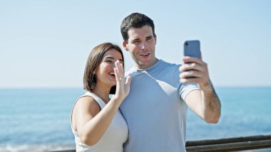 Güzel bir çift, deniz kenarında video görüşmesi yaparken gülümsüyor.