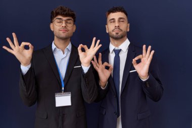 İki İspanyol iş adamı iş kıyafetleri giyip rahatlıyor ve gözleri kapalı gülümsüyor parmaklarıyla meditasyon hareketi yapıyorlar. yoga konsepti. 