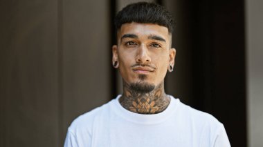 Sokakta ciddi bir ifadeyle dikilen genç Latin adam.