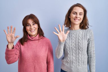 Anne ve kızı mavi arka planda durup parmaklarıyla on numarayı gösterirken kendinden emin ve mutlu bir şekilde gülümsüyorlar.. 