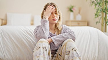 Young blonde woman stressed sitting on floor at bedroom