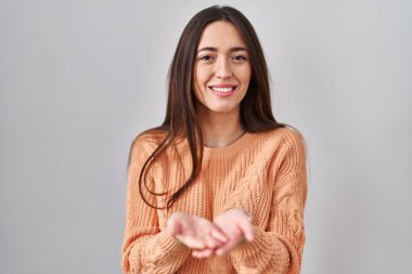 Beyaz arka planda duran esmer bir kadın avuçlarını birbirine uzatarak gülümsüyor ya da el hareketi yapıyor. Bekleme ve koruma 