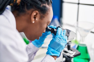 Laboratuvarda mikroskop kullanan Afrikalı Amerikalı kadın bilim adamı.