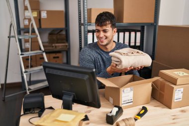 Young hispanic man ecommerce business worker preparing clothes package at office
