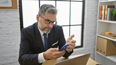 Yakışıklı, beyaz saçlı, üzgün, ofiste çalışan, akıllı telefondan mesaj atan ciddi bir iş adamı sorunlara konsantre oluyor.