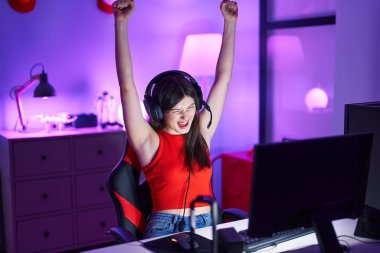 Young caucasian woman streamer playing video game with winner expression at gaming room