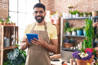 Young arab man florist smiling confident using touchpad at florist