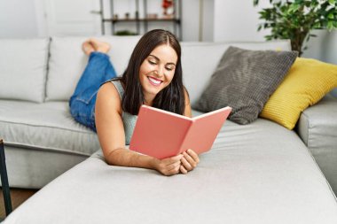 Evdeki kanepede uzanmış kitap okuyan güzel İspanyol kadın.