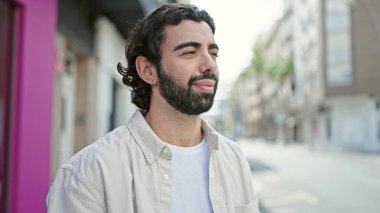 Latin kökenli genç adam ciddi bir ifadeyle sokağa bakıyor.