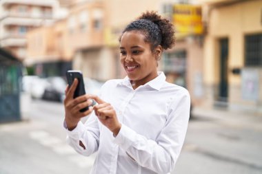 Afro-Amerikalı kadın sokakta akıllı telefon kullanarak kendine güveniyor.