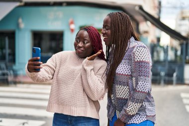 Afro-Amerikalı kadın arkadaşlar, sokakta video araması yaptıkları için gülümsüyorlar.