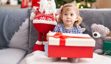 Sevimli İspanyol kız elinde hediyeyle evdeki Noel ağacının yanındaki koltukta oturuyor.