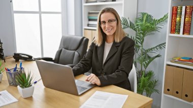 Kendine güvenen genç sarışın kadın, Joy 'un fotoğrafı, ofisteki dizüstü bilgisayarında pozitiflikle çalışıyor. Başarılı bir iş adamı, güzel ve başarılı, işinin dizginlerini zarif bir şekilde elinde tutuyor..