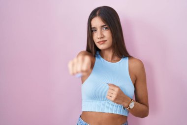 Genç esmer kadın pembe arka planda duruyor. Yumruk yumruğa dövüşmek, agresif ve öfkeli saldırı, tehdit ve şiddet. 