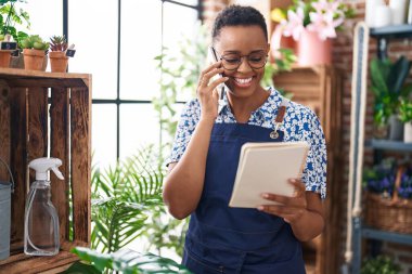 Afrikalı Amerikalı kadın çiçekçi çiçekçide akıllı telefondan not defteri okuyor.