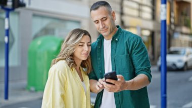Erkek ve kadın çift sokakta gülümseyen akıllı telefonları kullanarak yan yana dururlar.
