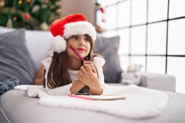 Adorable hispanic girl smiling confident lying on sofa by christmas tree at home