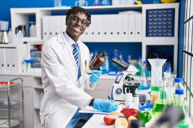 Afrikalı Amerikalı bilim adamı laboratuarda elinde şişeyle rapor yazıyor.