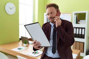 Orta yaşlı bir iş adamı ofisteki akıllı telefon okuma belgesiyle konuşuyor.