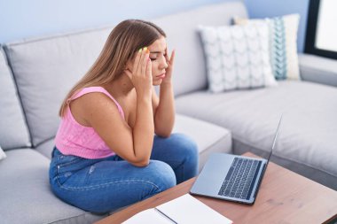 Young beautiful hispanic woman student sitting on sofa stressed at home