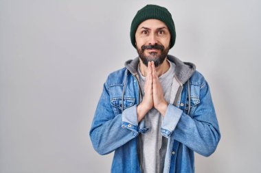 Dövmeleri olan, yün şapkalı, elleri birarada dua eden, affedilmek isteyen, kendine güvenen genç İspanyol bir adam.. 