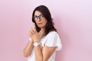 Orta yaşlı İspanyol kadın, günlük beyaz tişört ve gözlük takıyor. Sembolik bir silah taşıyor. El hareketleriyle cinayet silahlarıyla oynuyor. 