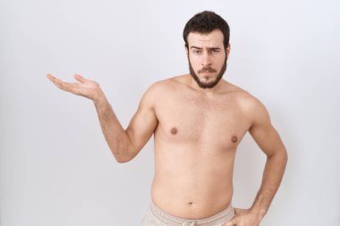 Beyaz arka plan üzerinde tişörtsüz duran genç İspanyol adam gülümseyen, eli avuçlarında kameraya bakan ve işaret eden.. 