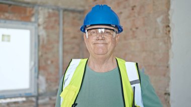 İnşaat alanında kendine gülen, orta yaşlı, gri saçlı bir inşaatçı.