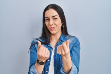 Mavi arka planda duran İspanyol kadın elleriyle para hareketi yapıyor, maaş istiyor, milyonerlik işi yapıyor. 