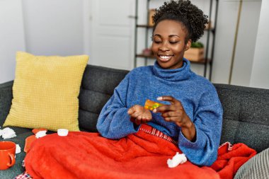 Afro-Amerikalı kadın evdeki kanepede oturup hap alıyor.