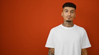 Ciddi yüz ifadesi olan havalı, genç Latin bir adam izole edilmiş kırmızı arka planda rahatlamış, sıradan ama konsantre bir yaşam tarzını canlandırıyor..