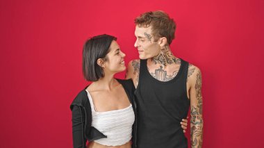 Güzel bir çift gülümsüyor. Birbirlerine sarılıyorlar ve izole edilmiş kırmızı arka planda birbirlerine bakıyorlar.