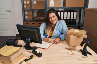 Young beautiful plus size woman ecommerce business worker writing on notebook working at office