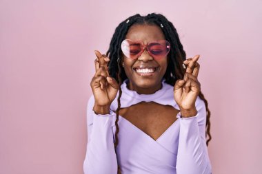 Pembe arka planda örülü saçları olan Afrikalı kadın umut ve gözleriyle gülümseyerek işaret ediyor. Şans ve batıl inançlar. 
