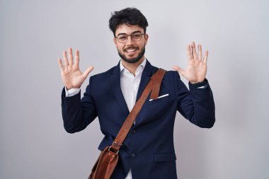 Sakallı, iş kıyafetleri giymiş İspanyol bir adam 10 numaralı parmaklarıyla gösteriş yapıyor ve gülümsüyor. Kendinden emin ve mutlu.. 