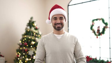 Evde Noel ağacının yanında kendinden emin gülümseyen genç İspanyol adam.