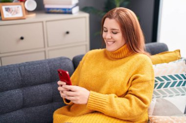 Young beautiful plus size woman using smartphone sitting on sofa at home