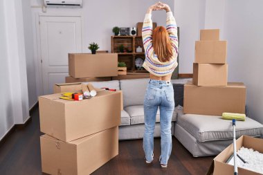 Young caucasian woman stretching arms standing on back view at new home