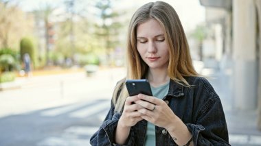Sokakta ciddi yüzlü akıllı telefon kullanan genç sarışın kadın.